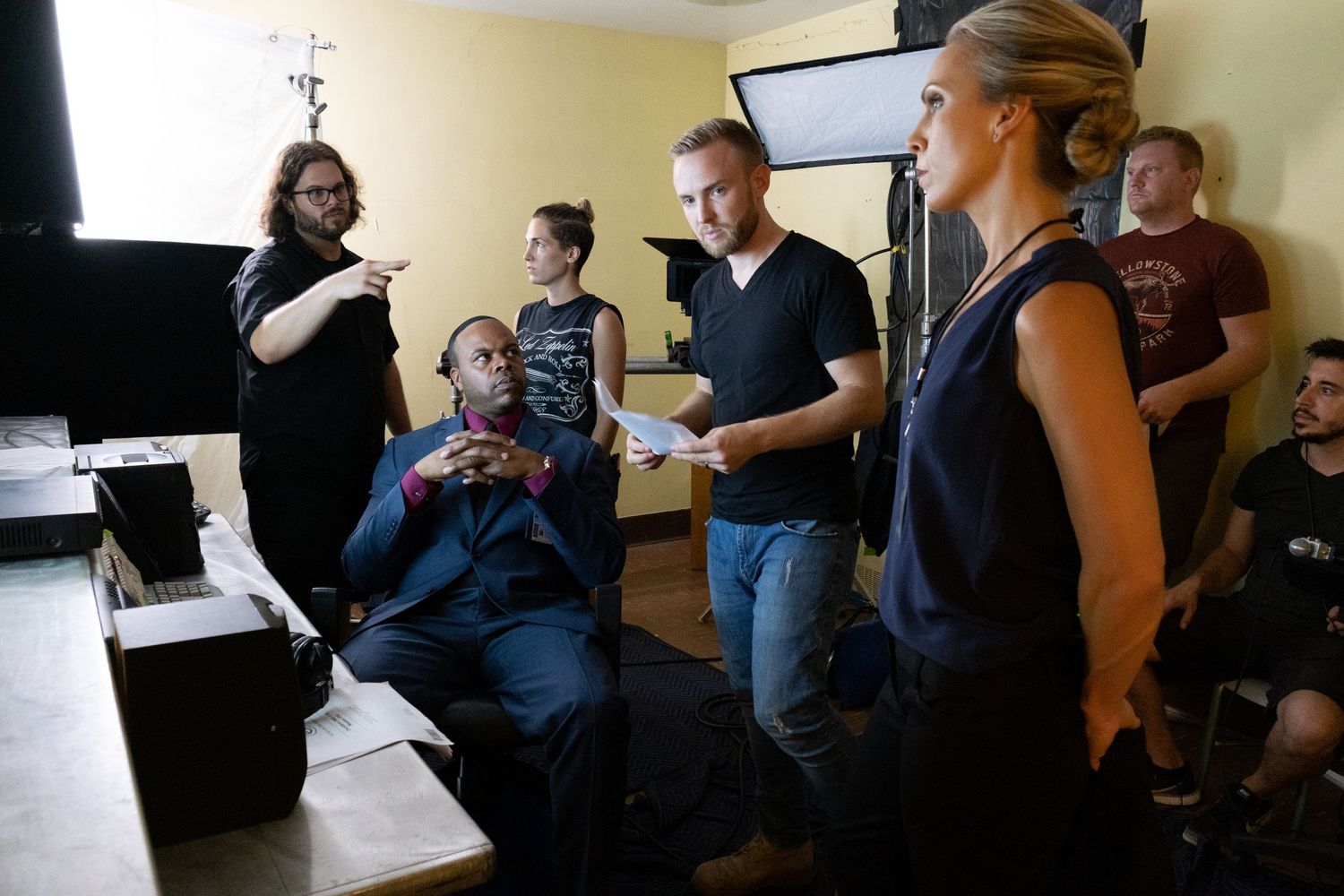 A diverse group of film crew members collaborate in a room with lighting equipment during a video production shoot.