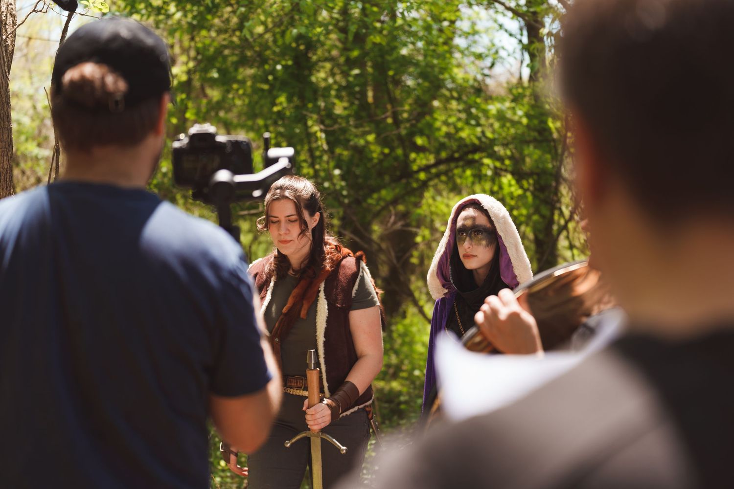 Film crew working outdoors in a wooded area with natural lighting and camera equipment.