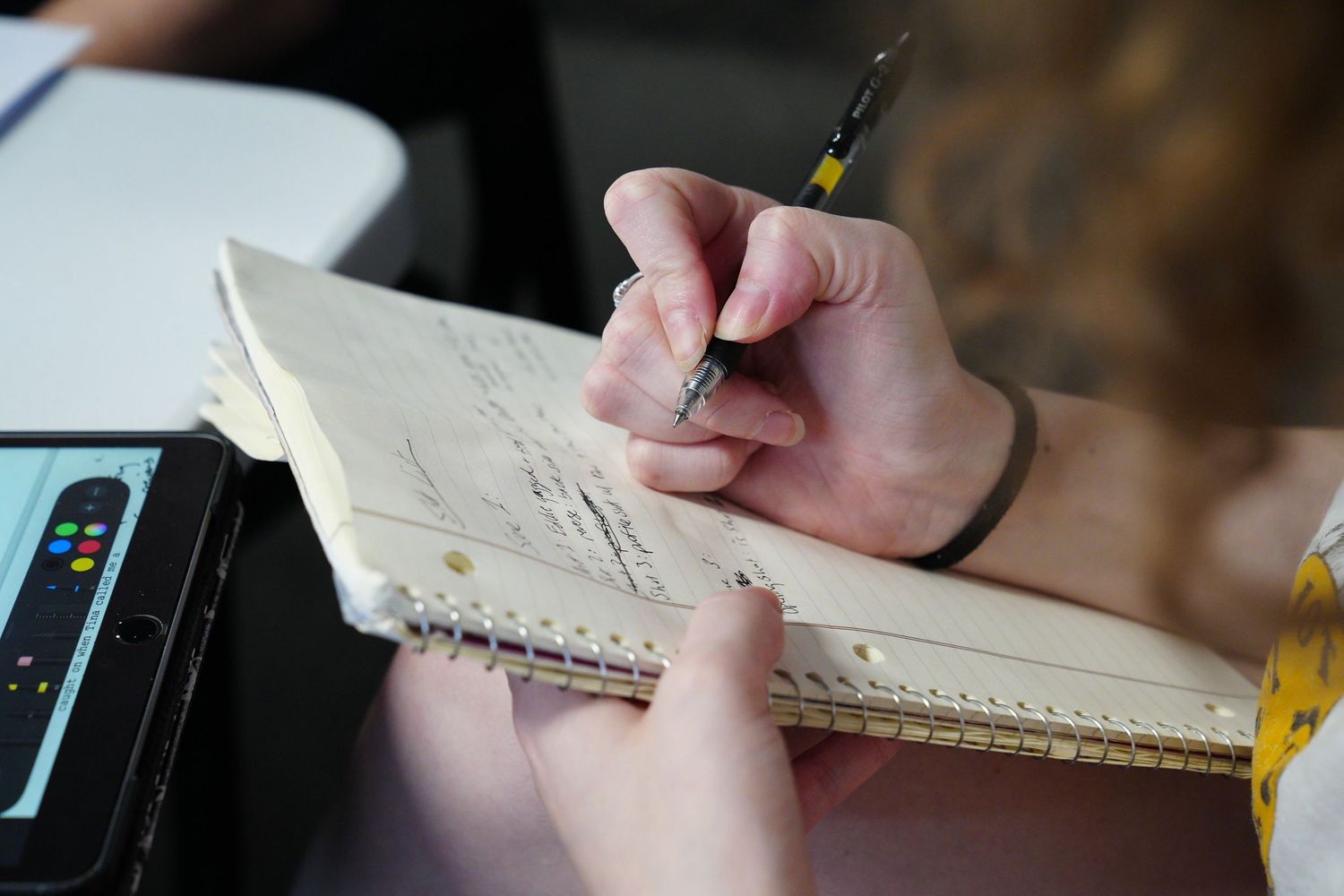 Close-up of hands writing notes in a spiral notebook with a pen at a desk.
