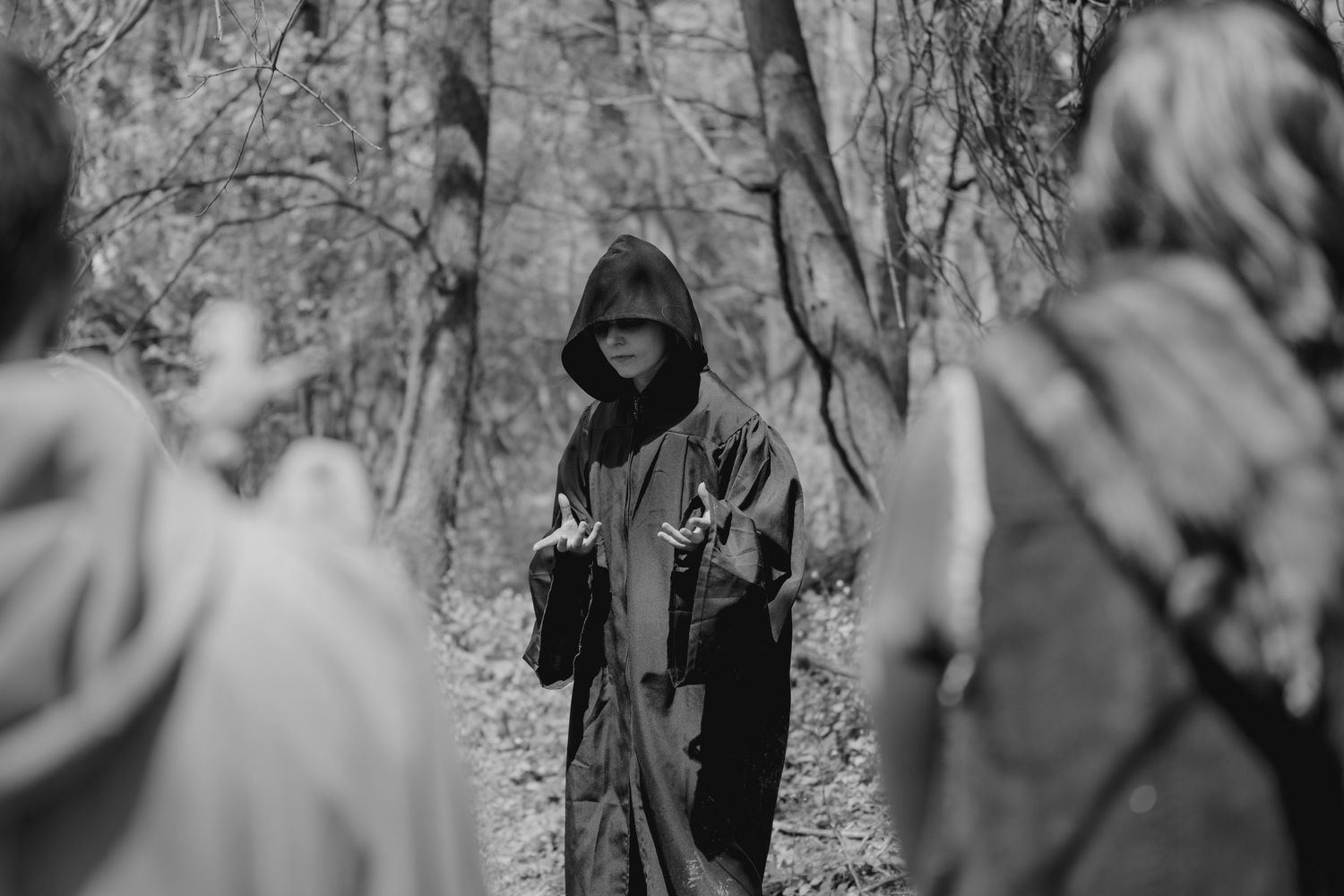 Blurred black and white image of people gathered in a wooded setting.