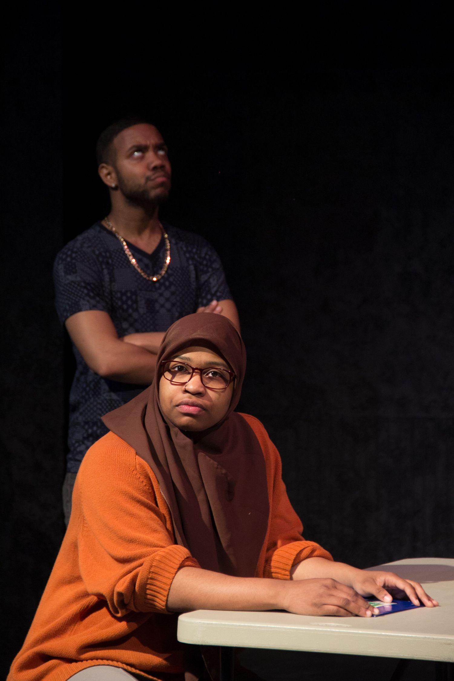 Student in orange attire sitting at desk during dramatic scene.