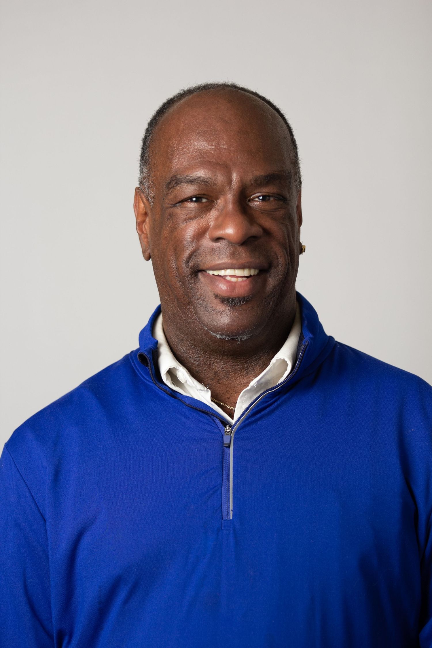 Professional headshot of someone wearing a bright royal blue quarter-zip pullover and white collar shirt against gray background.
