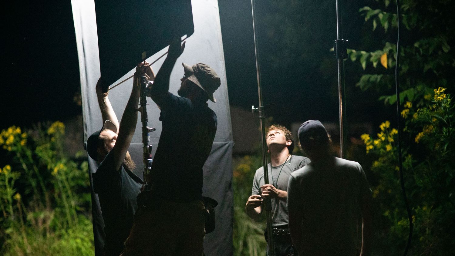 Film crew adjusting lighting equipment outdoors at night during a movie or video production shoot.