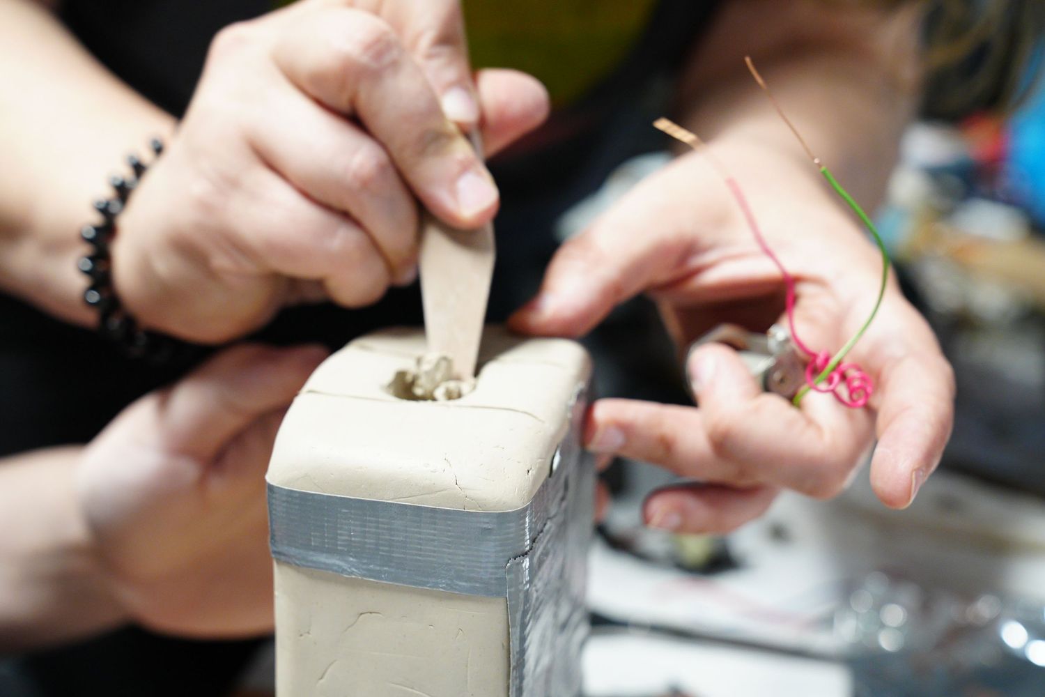 Close-up of hands carefully crafting jewelry using tools and colorful thread on a small block.