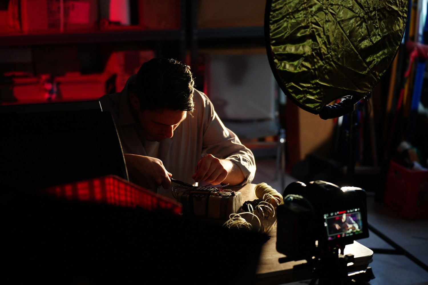 Person working at a dimly lit desk with a camera in the foreground and a softbox light in a dark studio.