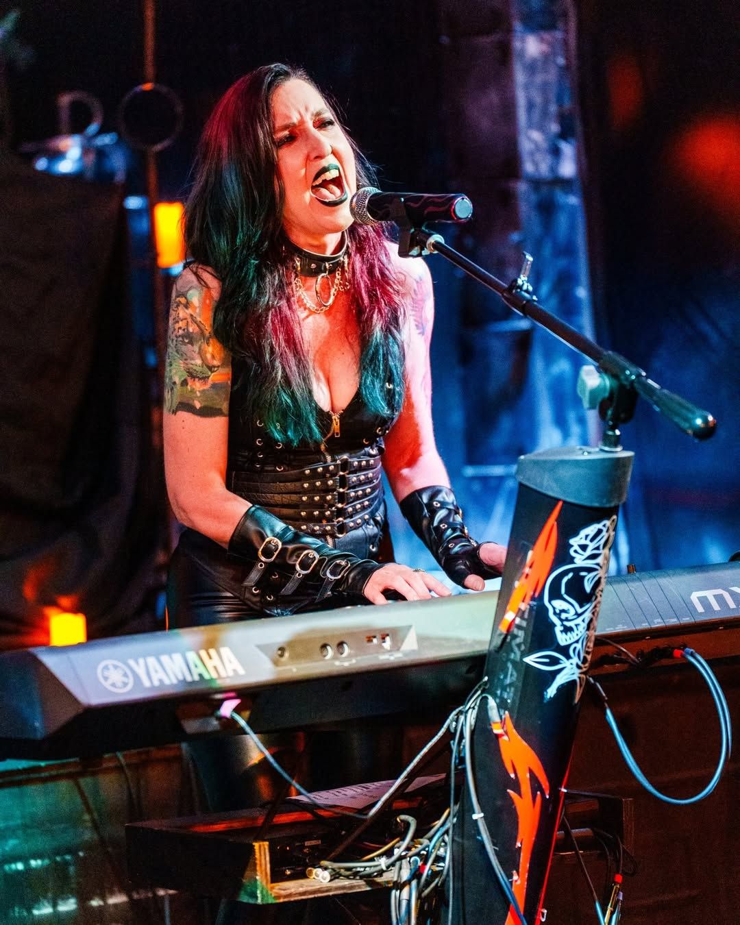 Musician performing energetically at a keyboard on stage with dramatic blue and red lighting.