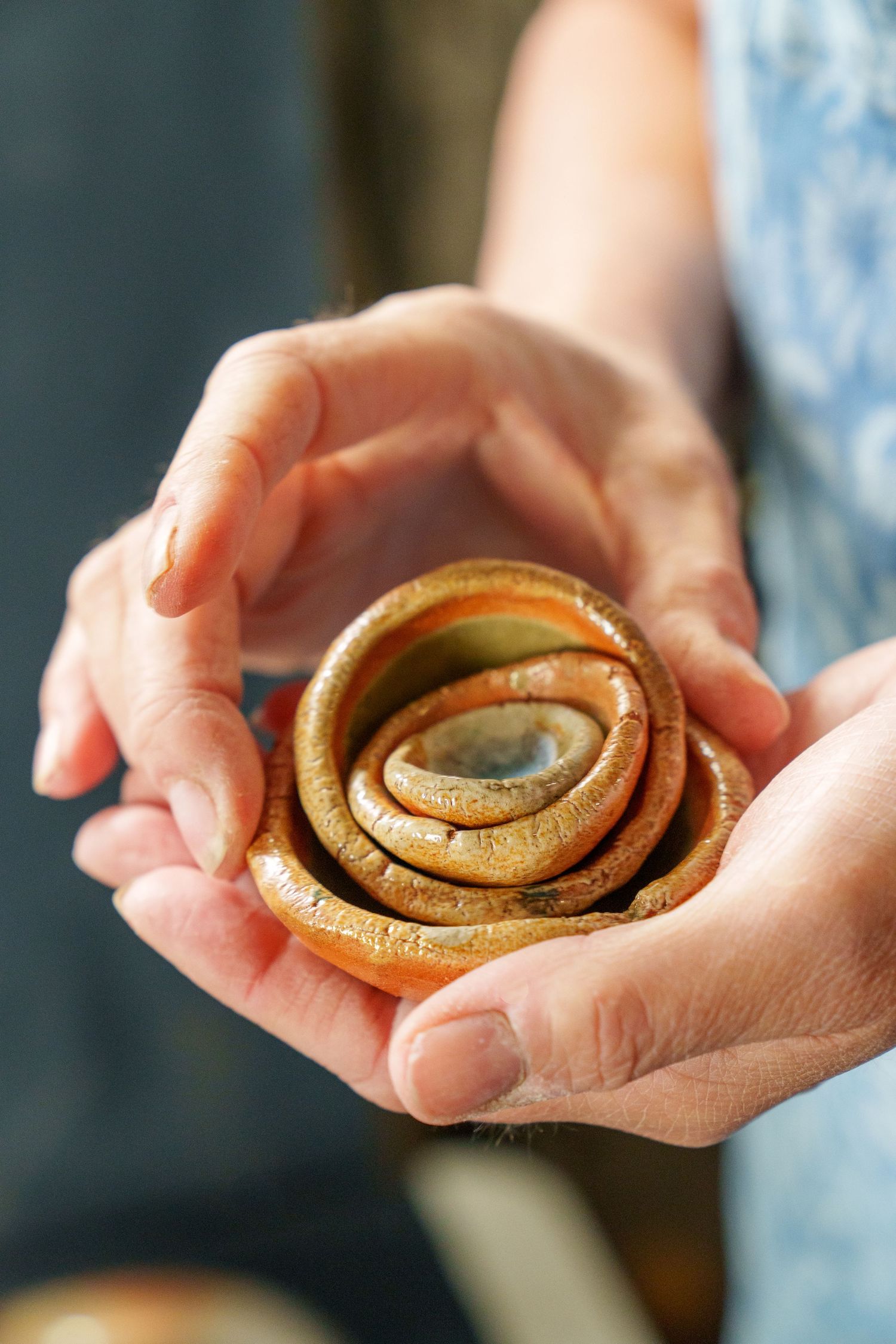 Hands holding a freshly baked cinnamon roll with swirled layers of dough and spices visible from different angles.
