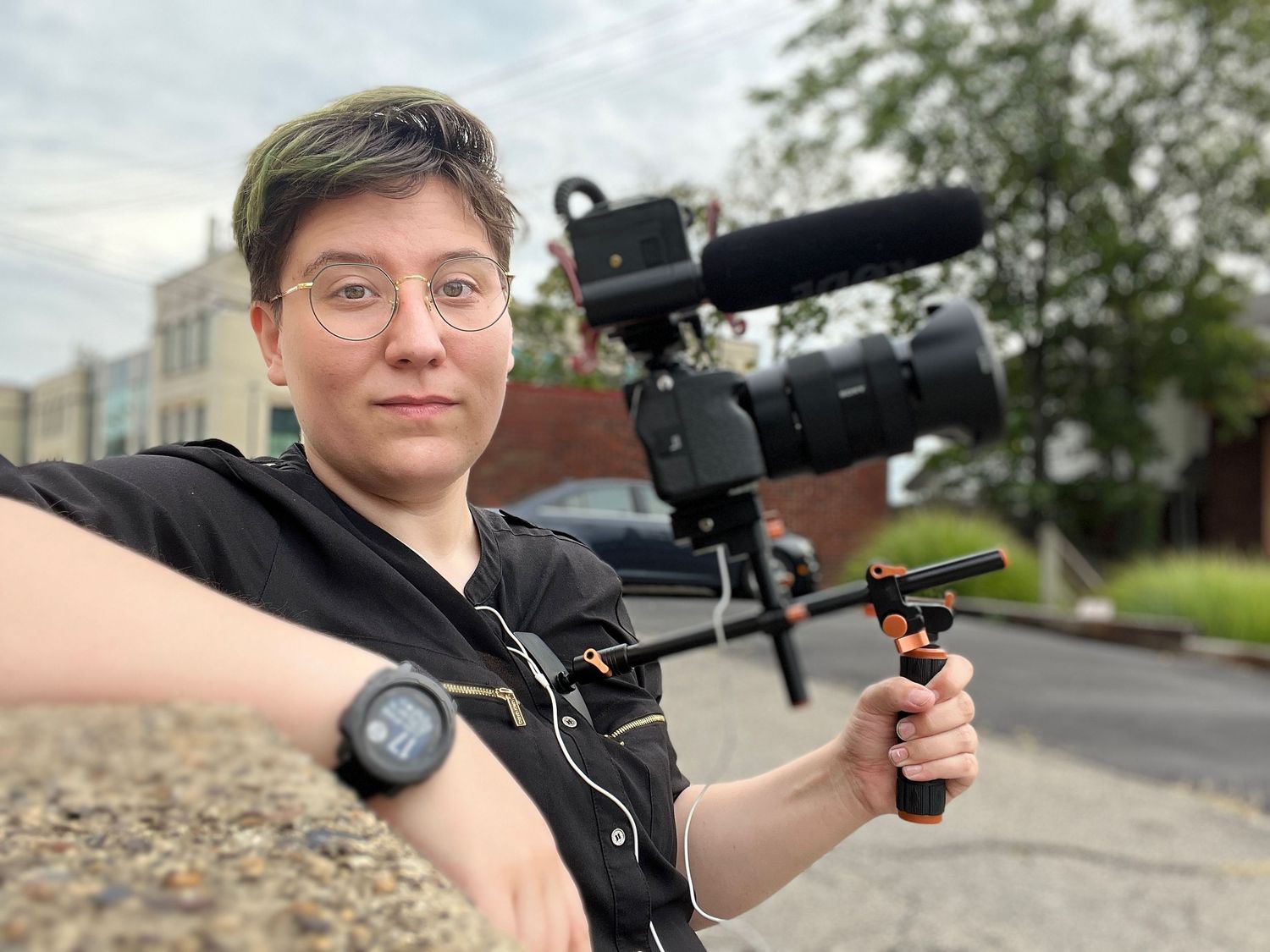 Person demonstrating camera equipment outdoors on cloudy day.