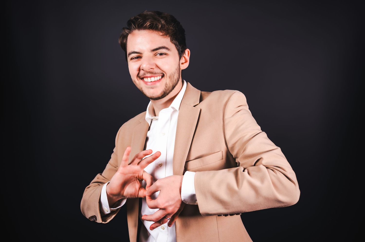 Person in tan suit jacket makes a series of expressive gestures and poses against dark background.