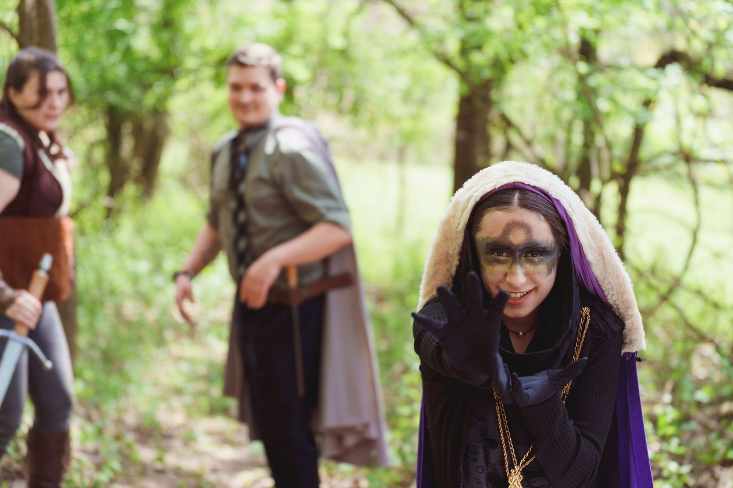 Group of people in costume gather along a wooded path during an outdoor event.