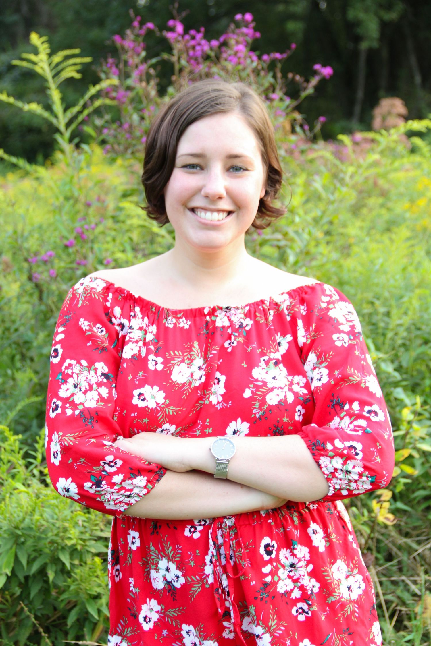 Red floral dress styled against garden background with purple flowers.