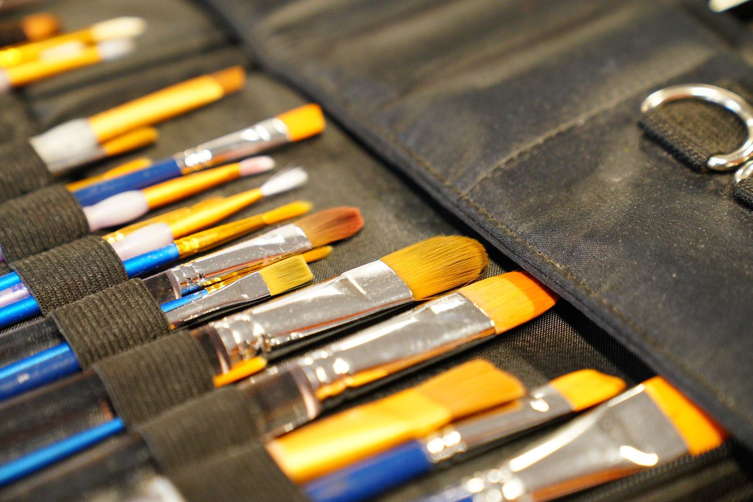 Set of professional artist paint brushes with yellow handles organized in a black canvas roll case.