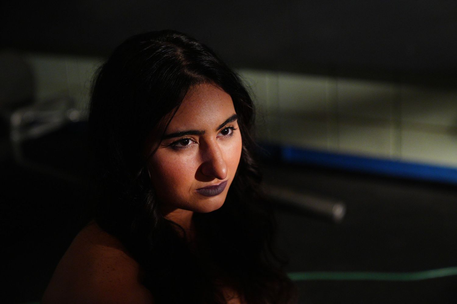 Young woman with dark hair and blue lipstick in dramatic low-key lighting.