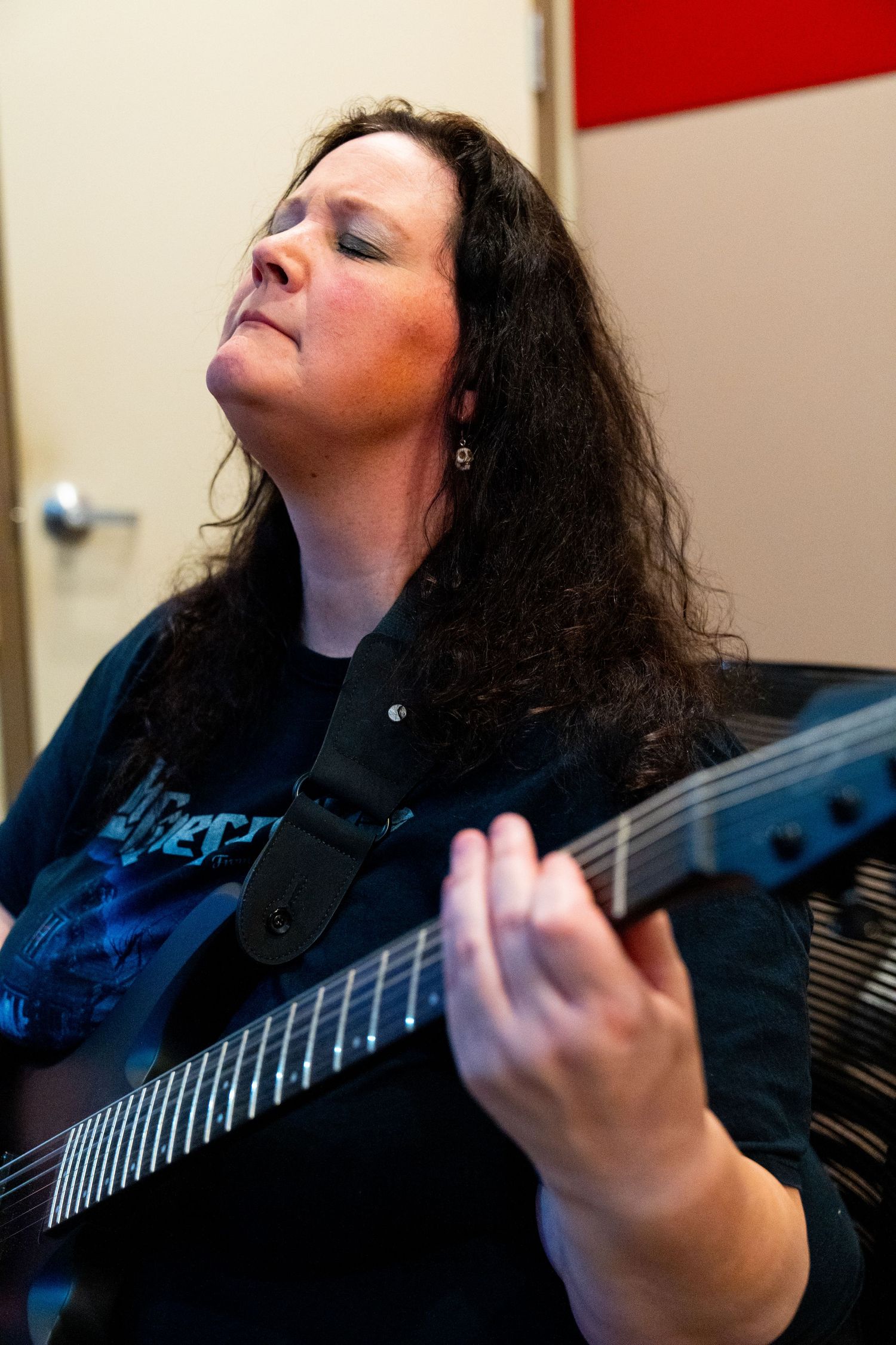 Musician playing electric guitar with intense expression and long dark hair.