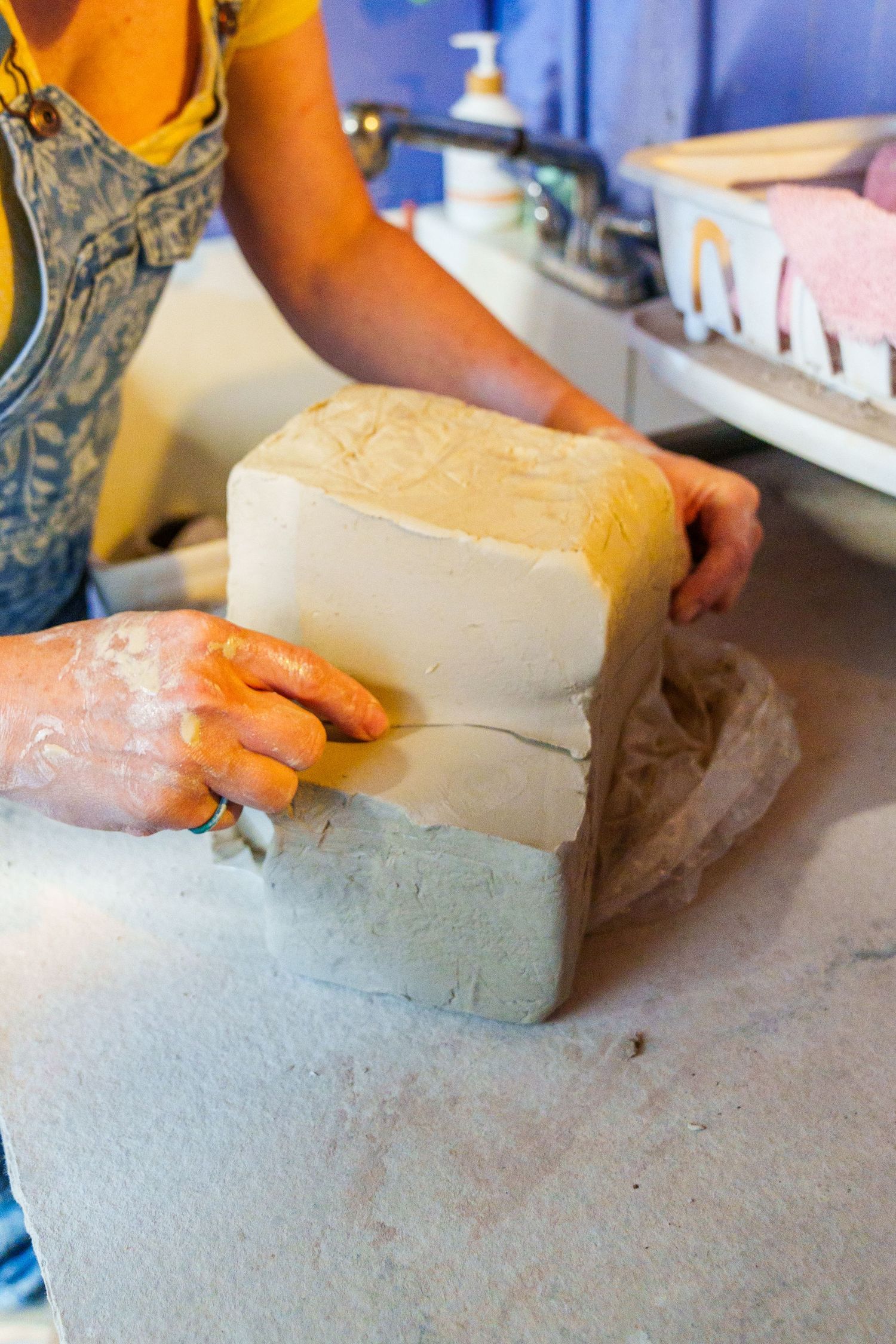 Hands working with blocks of clay on a counter surface while wearing orange gloves.