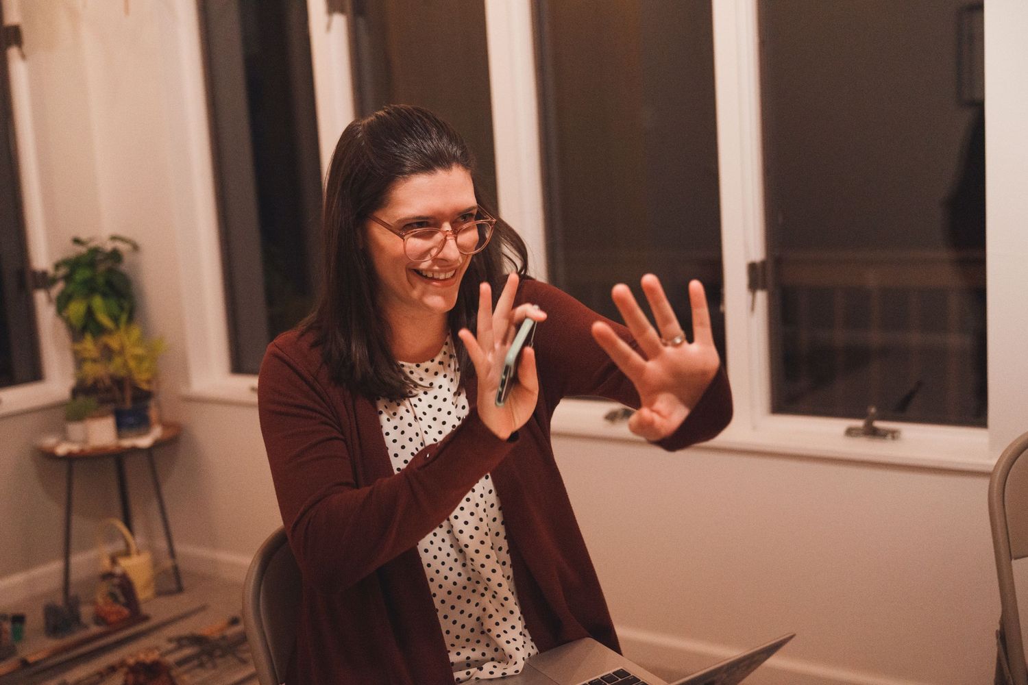 Person in burgundy cardigan making expressive hand gestures while speaking.