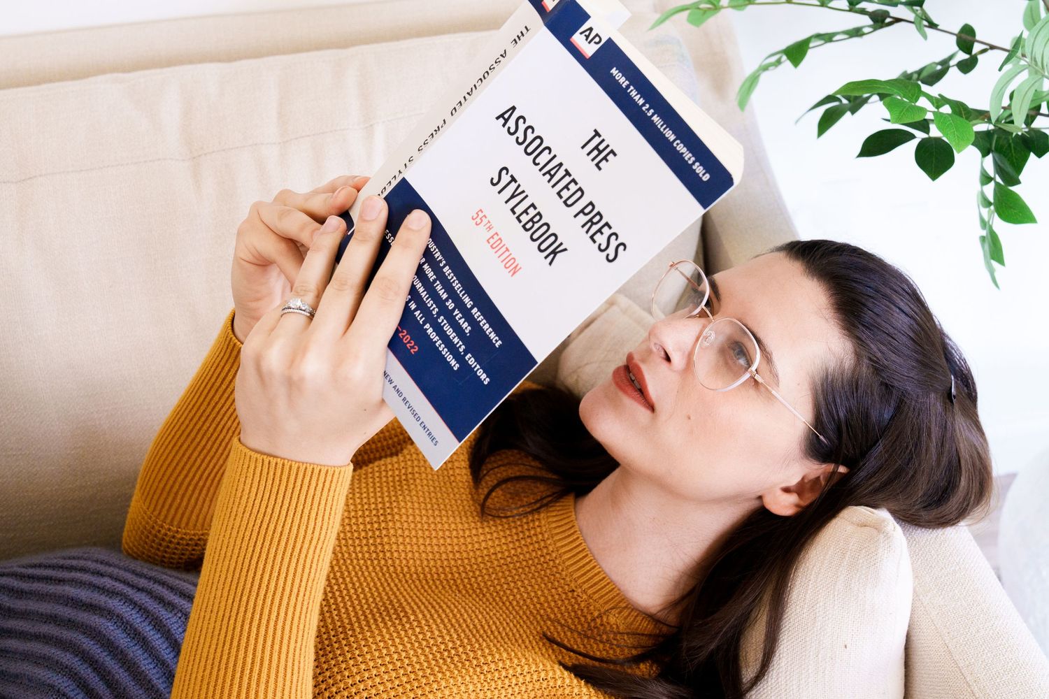 Someone reading a book while lying on couch with decorative plants nearby.