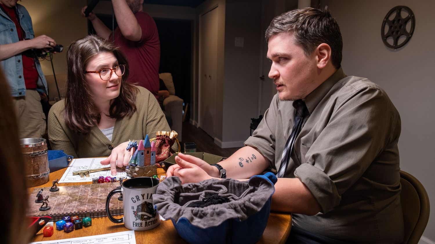 Two people playing Dungeons and Dragons at a table with dice and miniatures in a dimly lit room.
