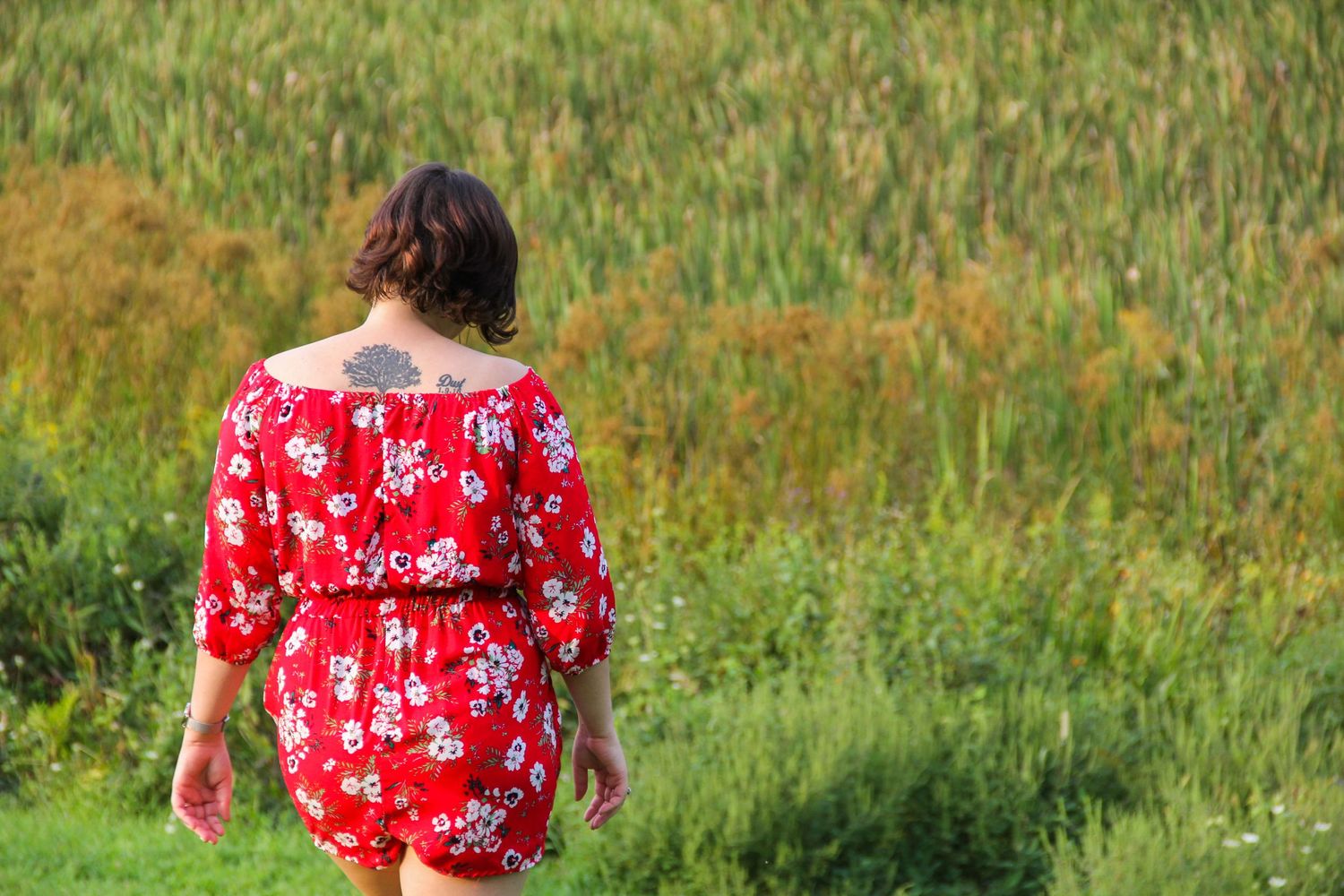 Red floral dress shown from behind against green grass field.