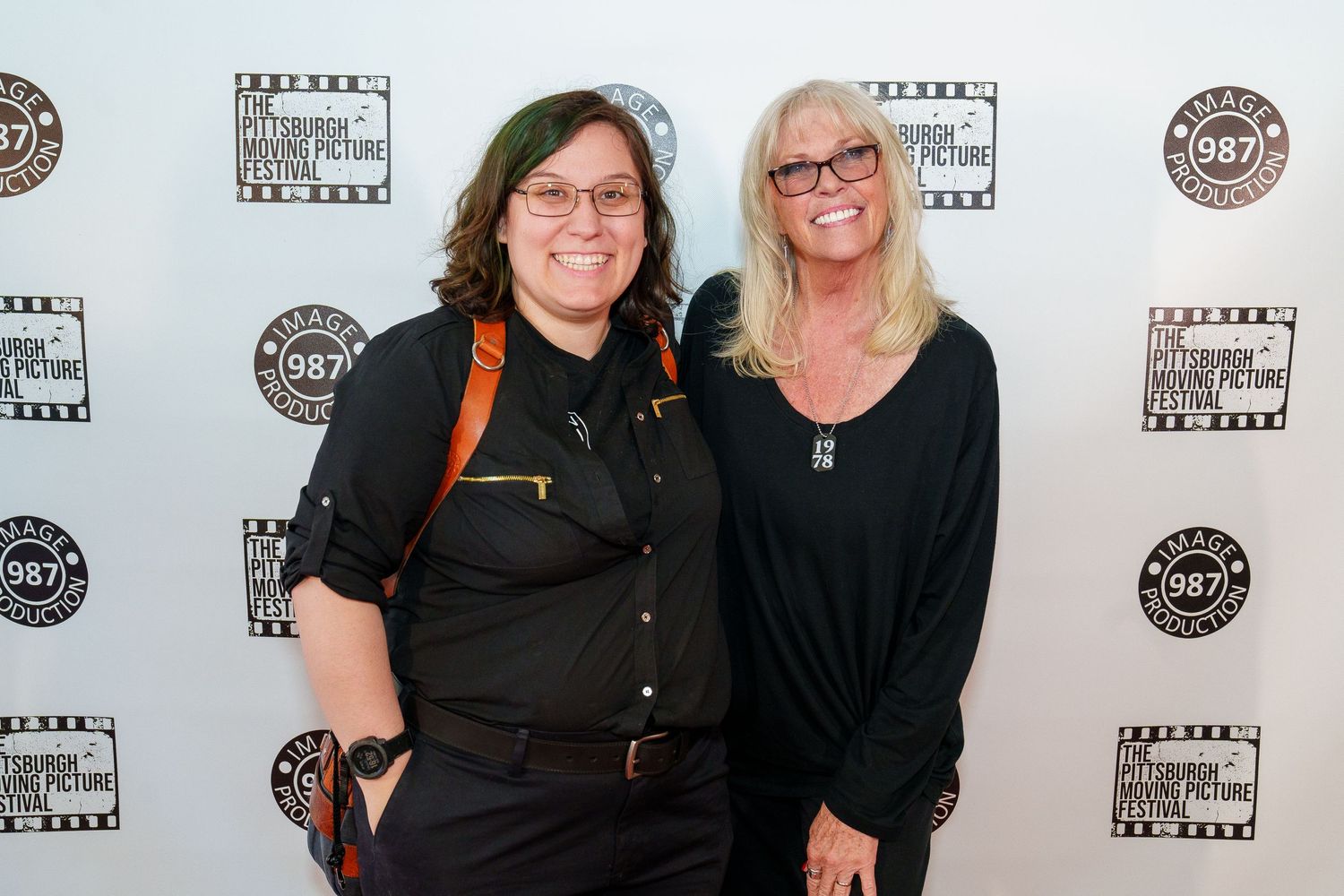 Two people pose together at a film industry event with banners and logos visible in the background.