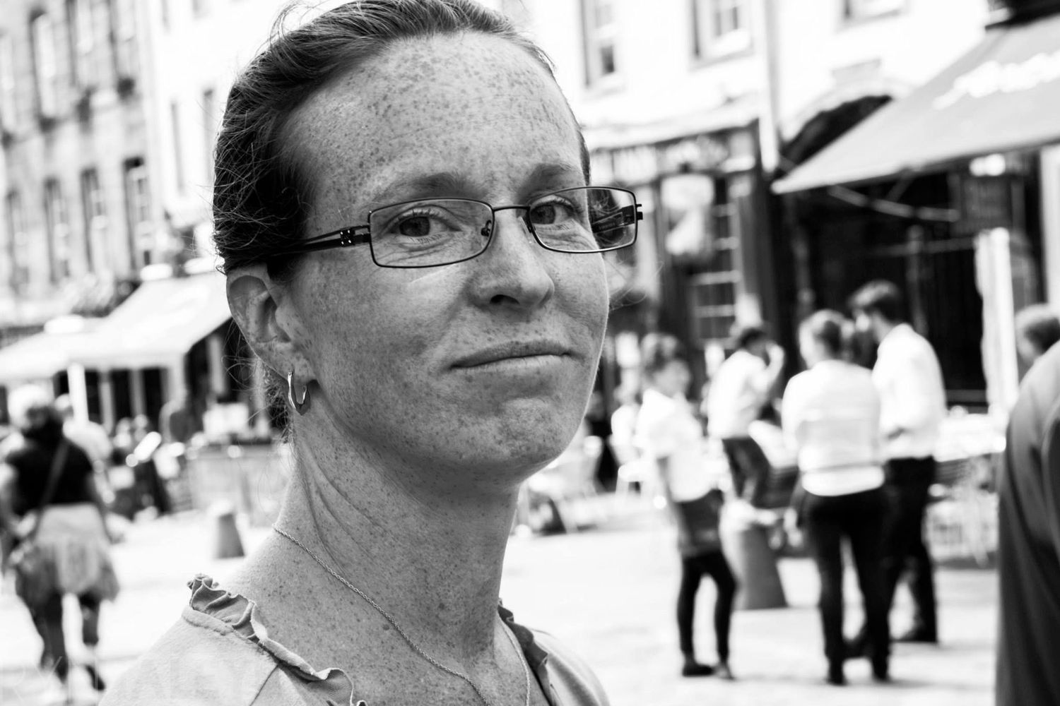A black and white collage of candid portraits showing someone in glasses against various urban backgrounds.