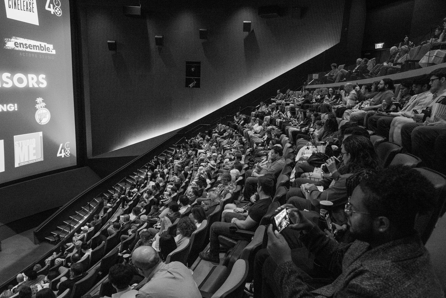 A packed audience fills a dark theater during a film screening or presentation.