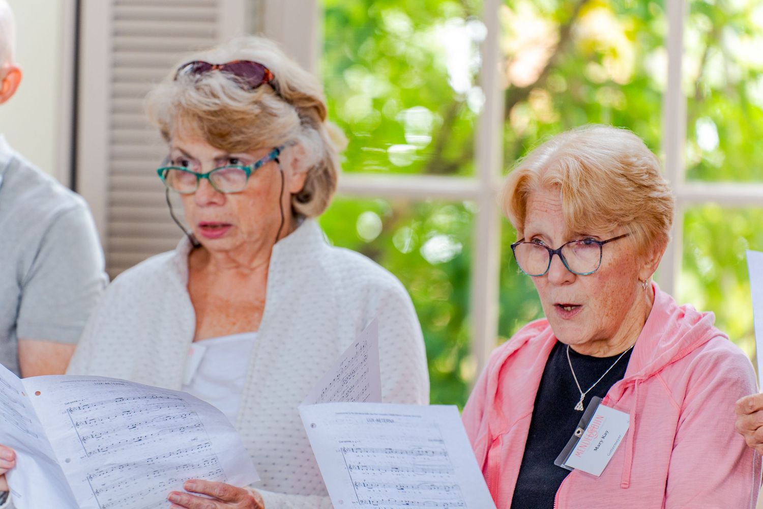 Several people in casual attire reading from papers while seated outdoors.