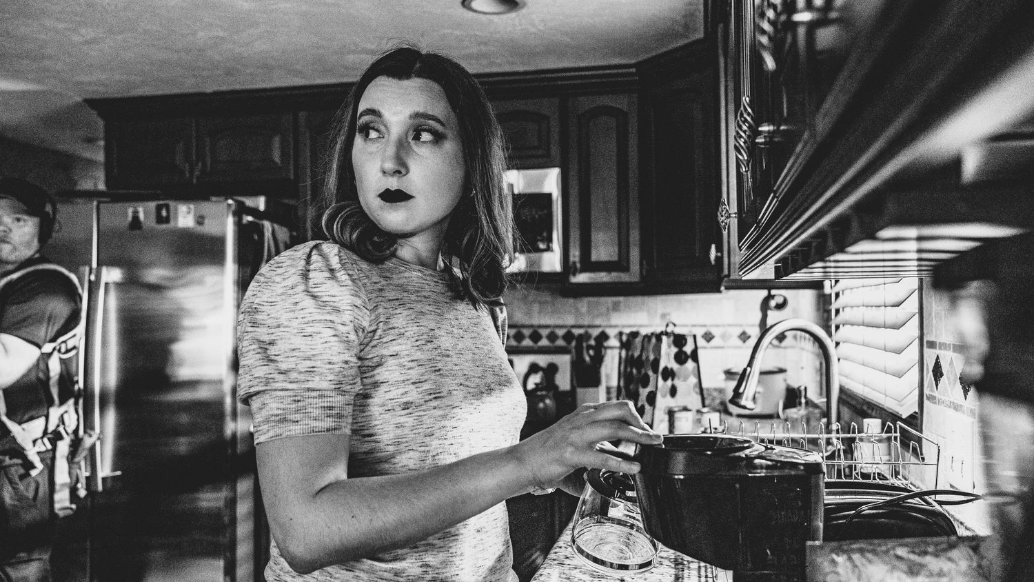 A person wearing a floral dress prepares drinks behind a bar counter in black and white photography.
