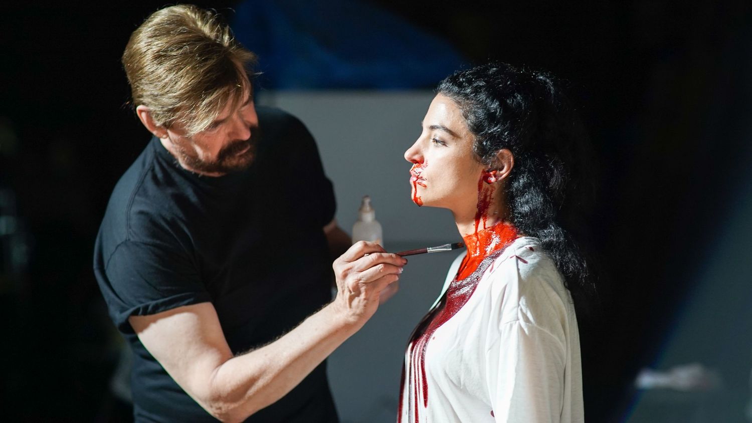 Makeup artist applying cosmetics to performer backstage.