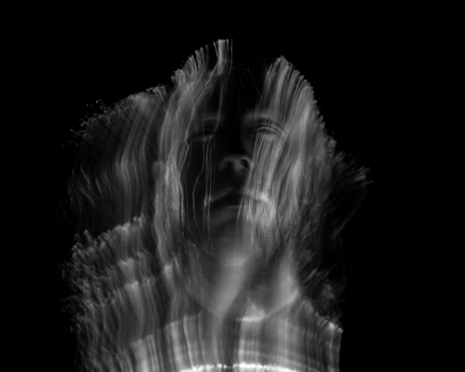 Monochrome light trails forming a feathery pattern against a dark background.
