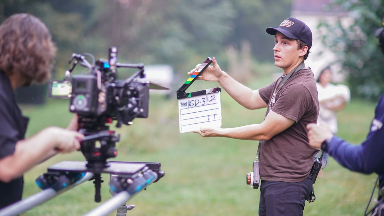A film crew member holds a clapperboard on an outdoor movie set with a camera.