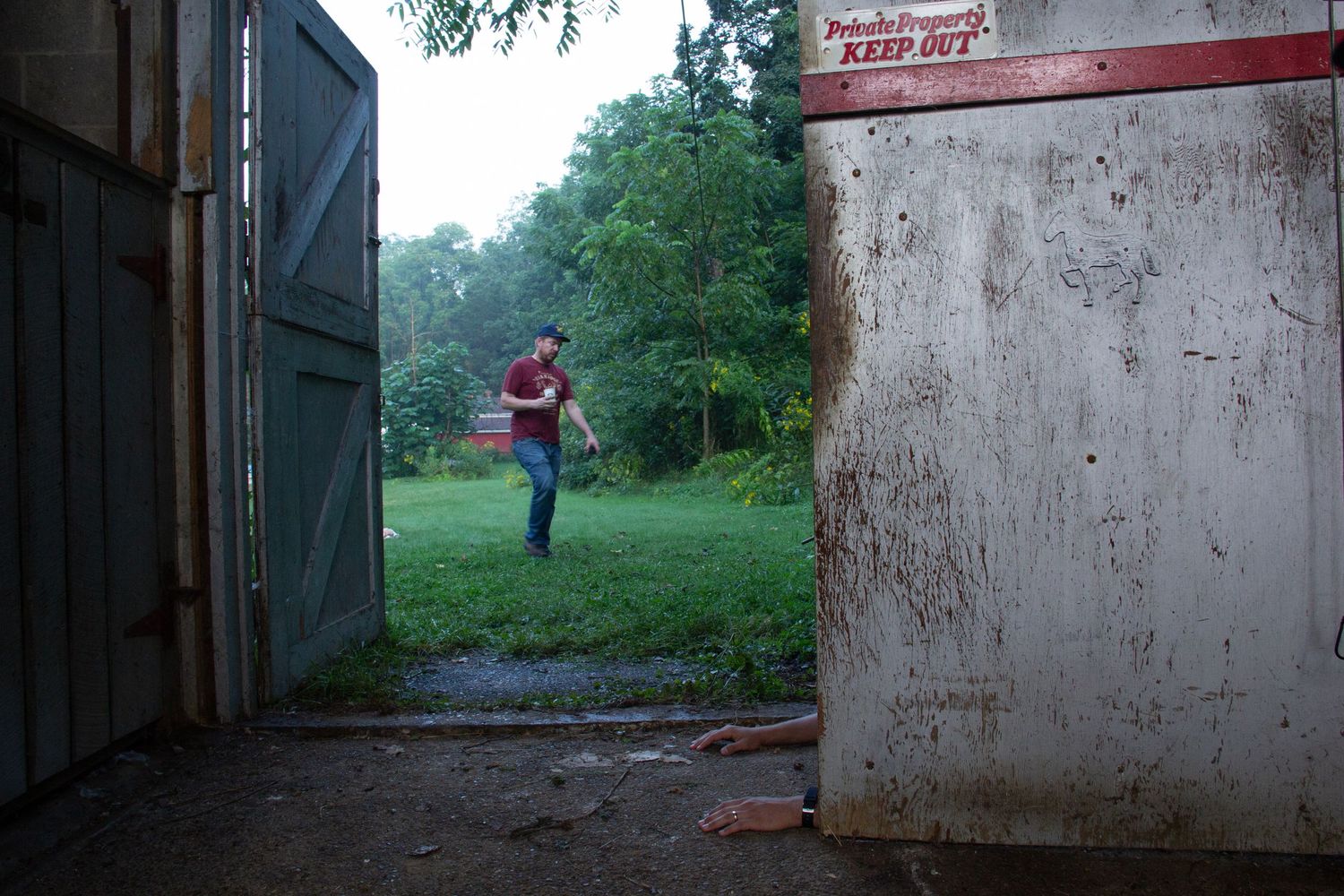 Man carrying a box walks toward a barn entrance with a Private Property Keep Out sign on a rainy day.