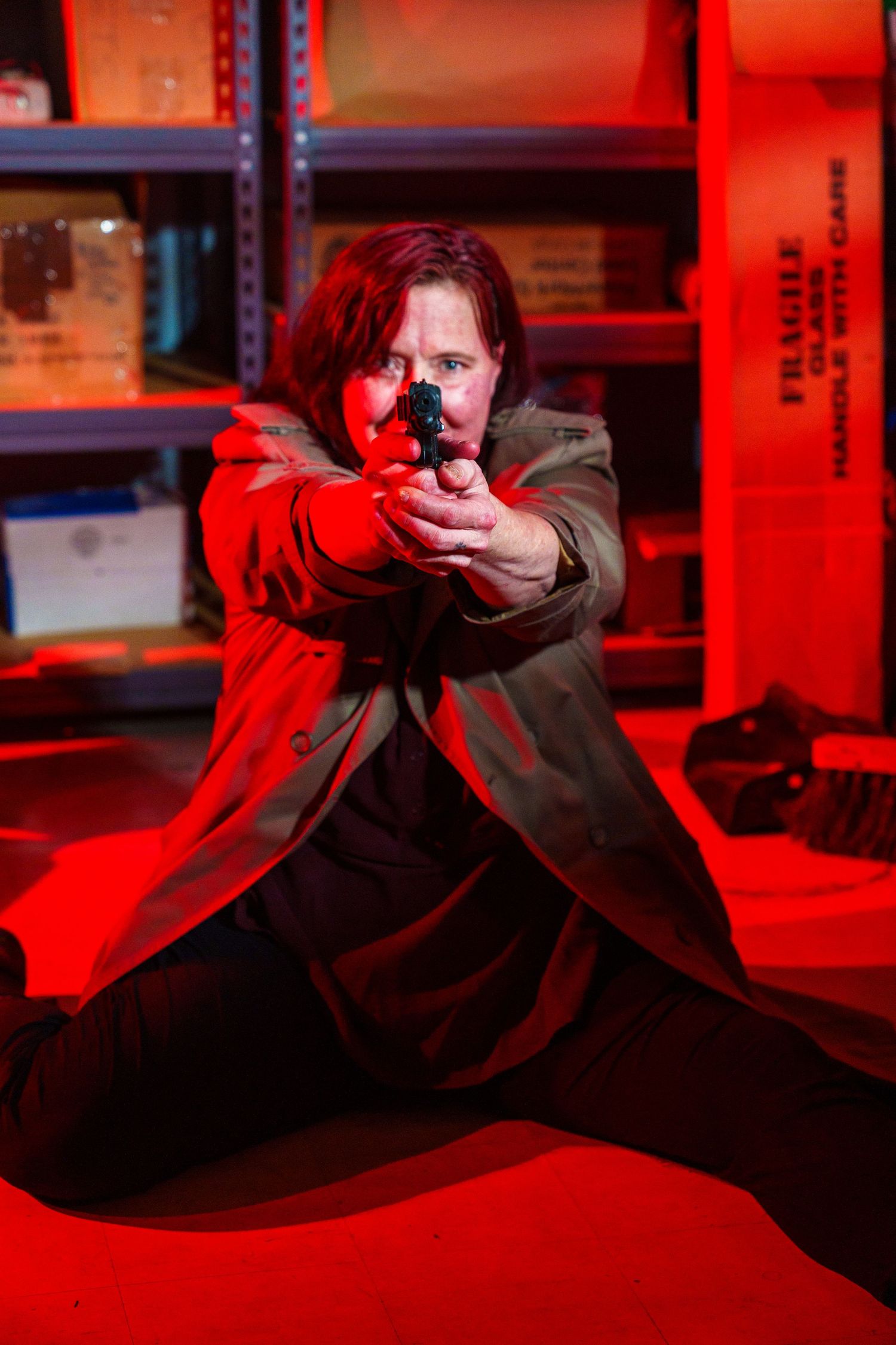 Person in a dark coat aiming with dramatic red lighting in an industrial setting.