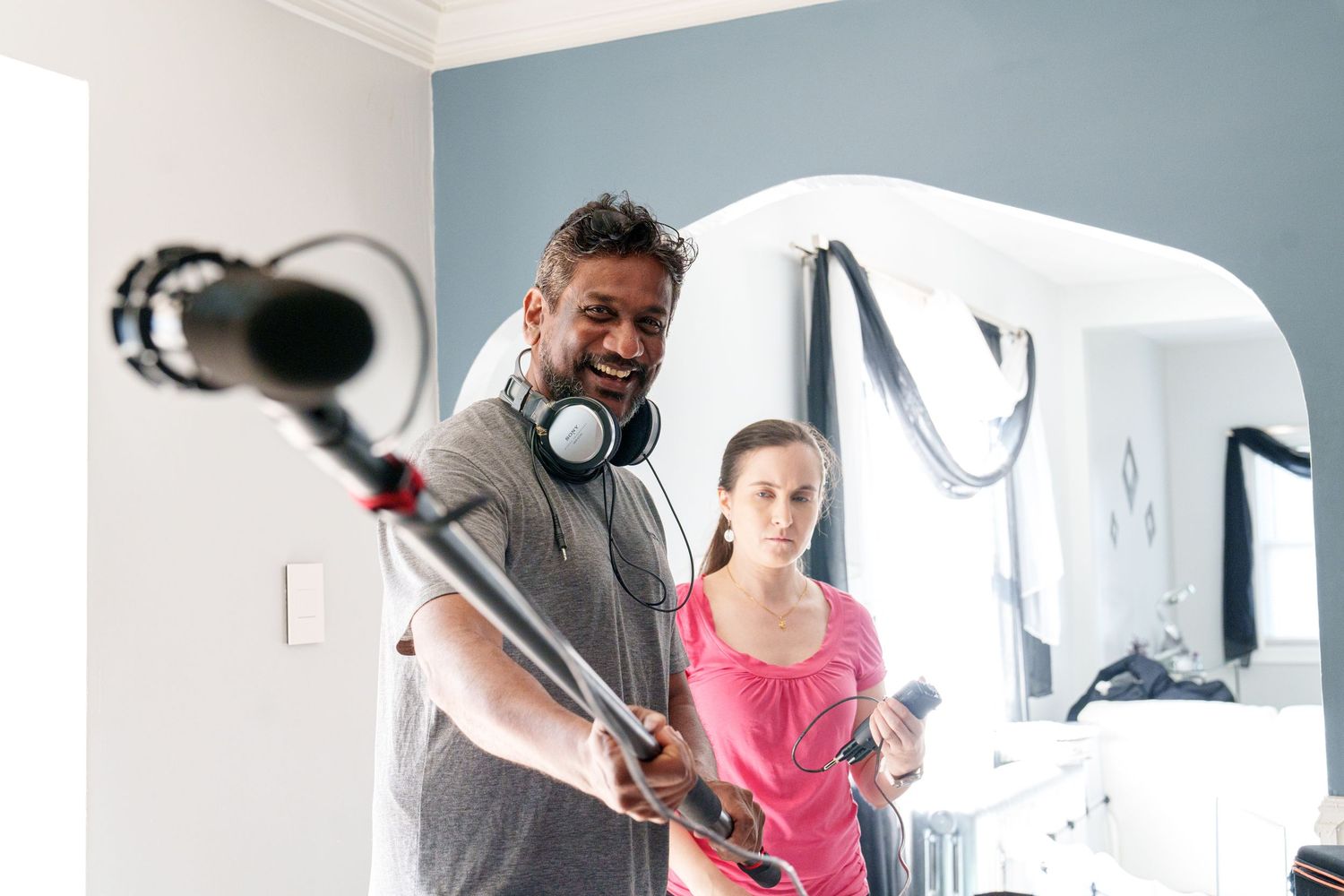 Man with headphones holds boom microphone while woman in pink assists indoors.