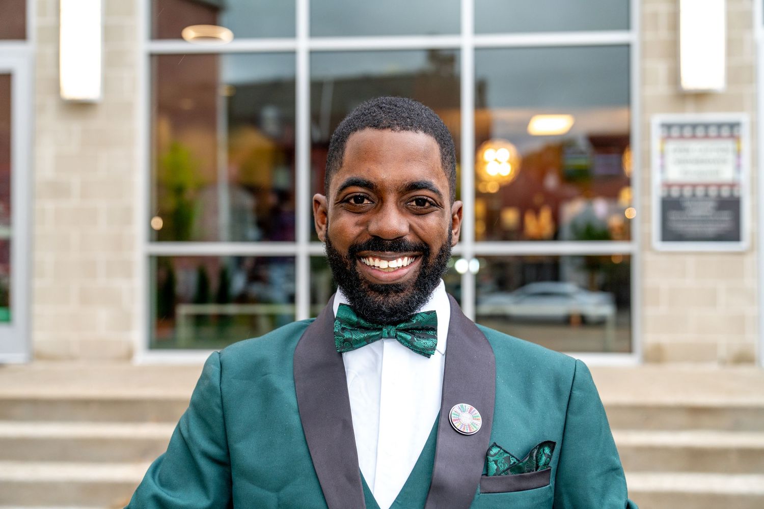 Three people in green blazers and bow ties smile warmly while standing together at a formal event.