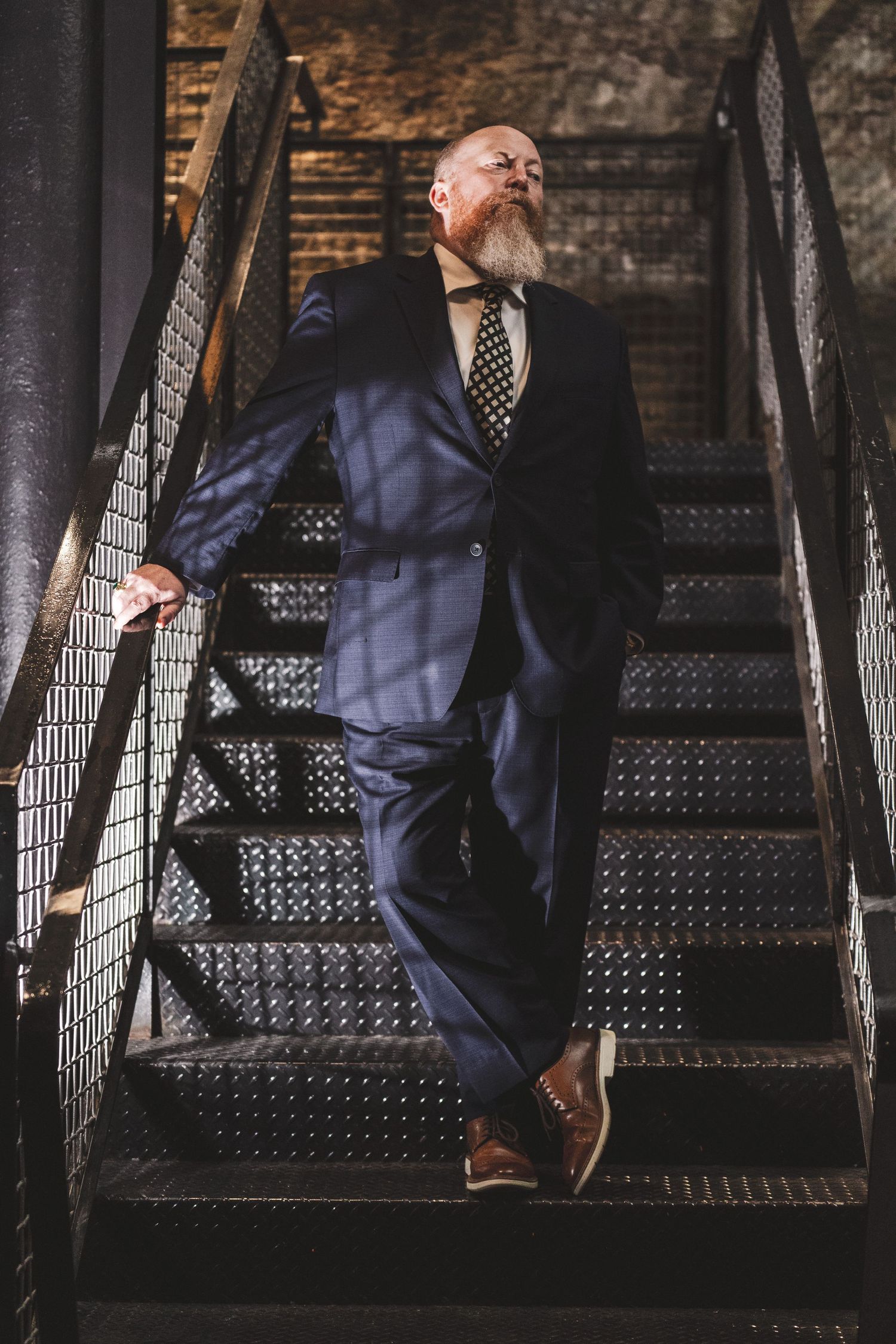 Close-up view of person in navy suit and polka dot tie walking down black metal industrial staircase.