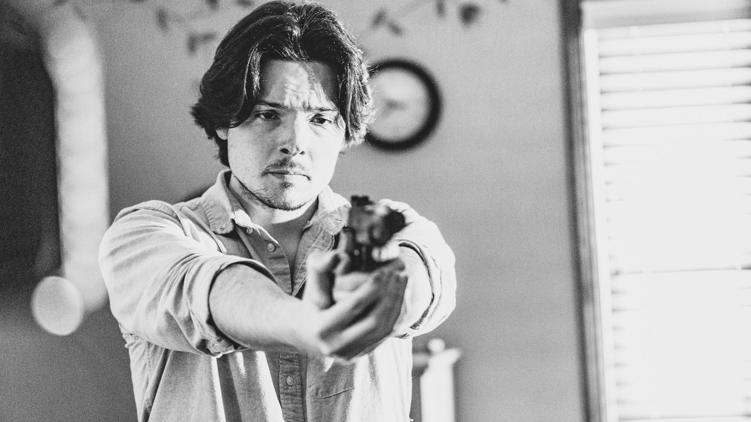 Cinematic black and white scene of person aiming handgun at camera.