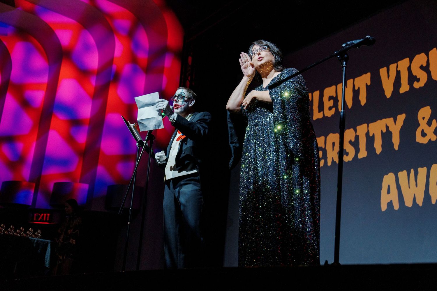 Stage performance with colorful lighting and projected text visible in background.