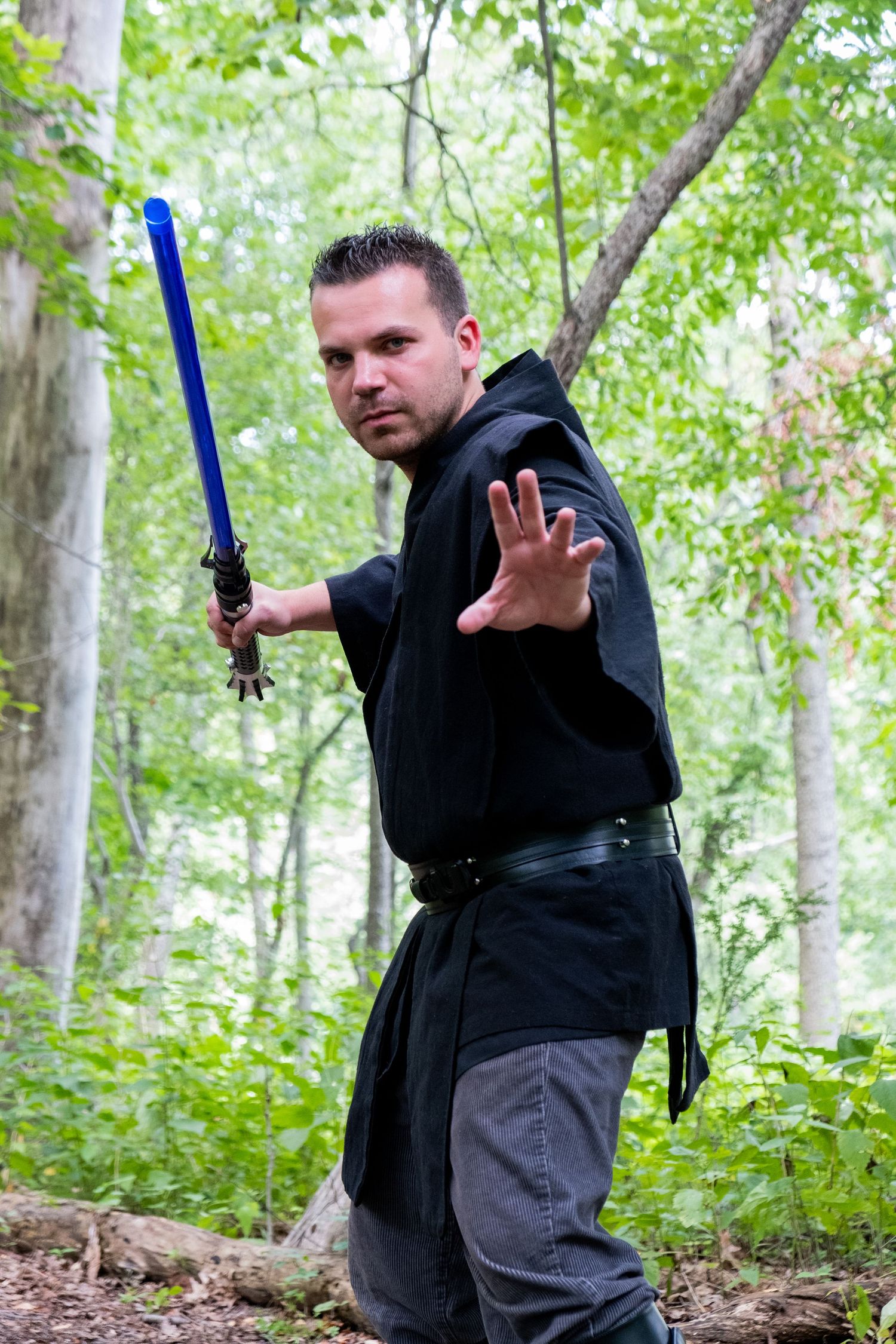 A series of action poses showing someone in dark clothing wielding a blue lightsaber in the woods.