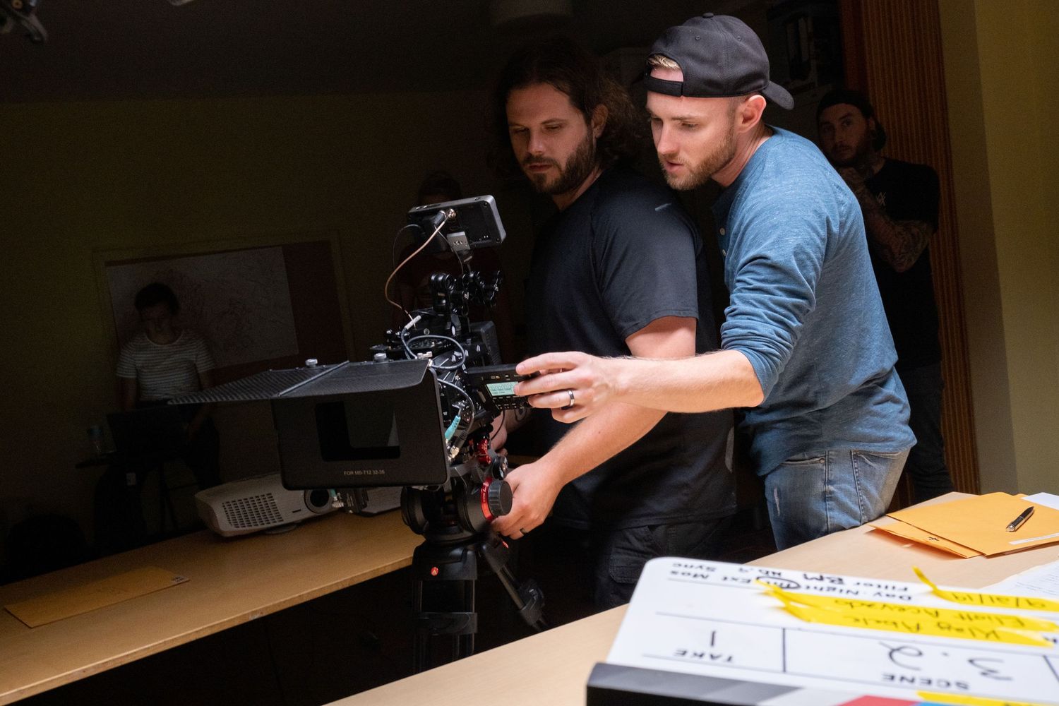 Two male filmmakers adjust a professional camera rig on a dimly lit film production set.
