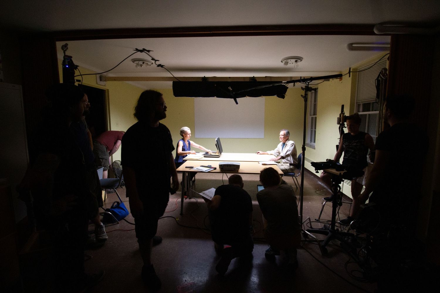 Behind the scenes of a film production with crew members gathered around a lit table in a dark room.