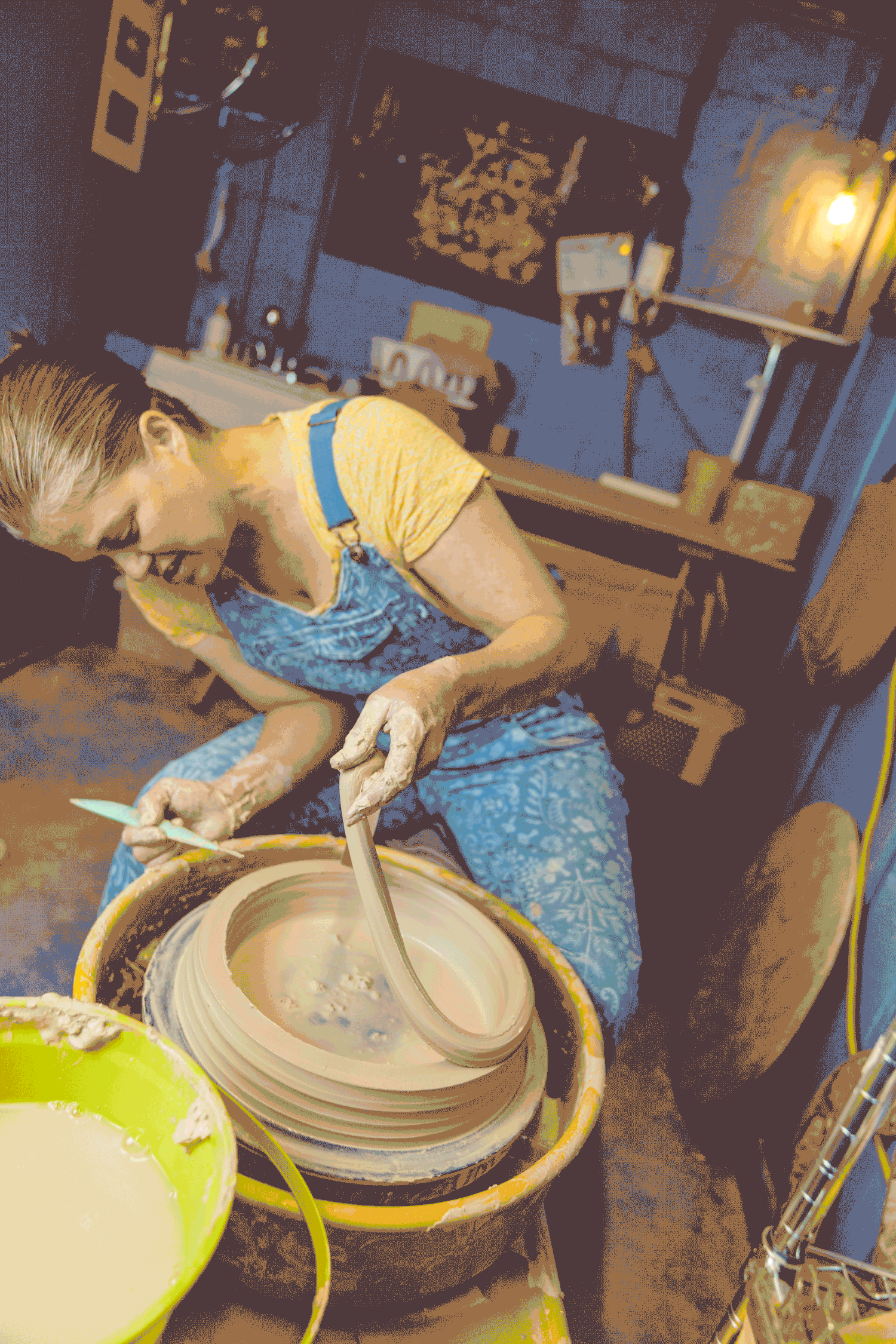A person in a blue dress shapes clay on a pottery wheel during a ceramics class.