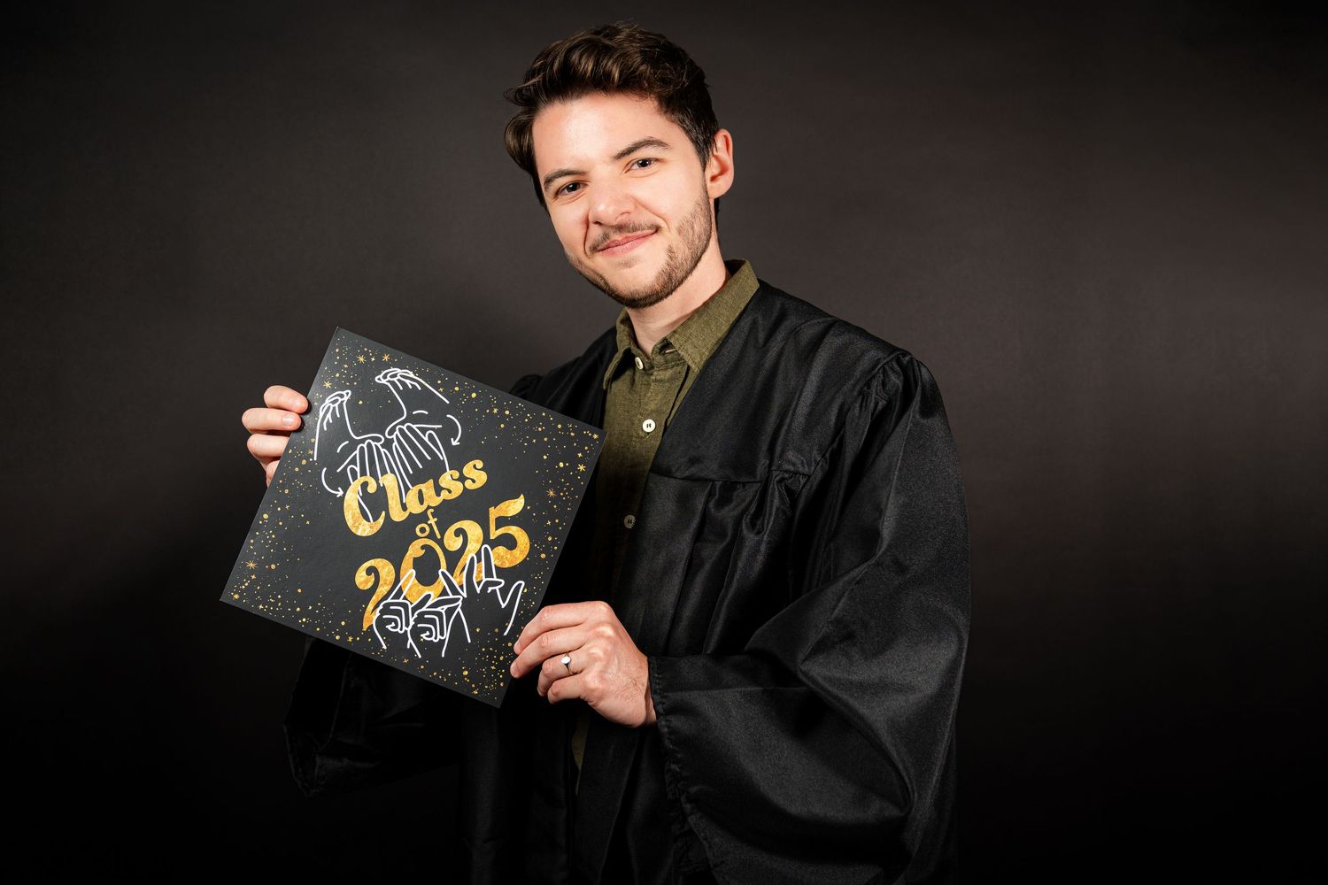 A graduate in black academic regalia holds a diploma and poses for celebratory graduation photos against a dark background.