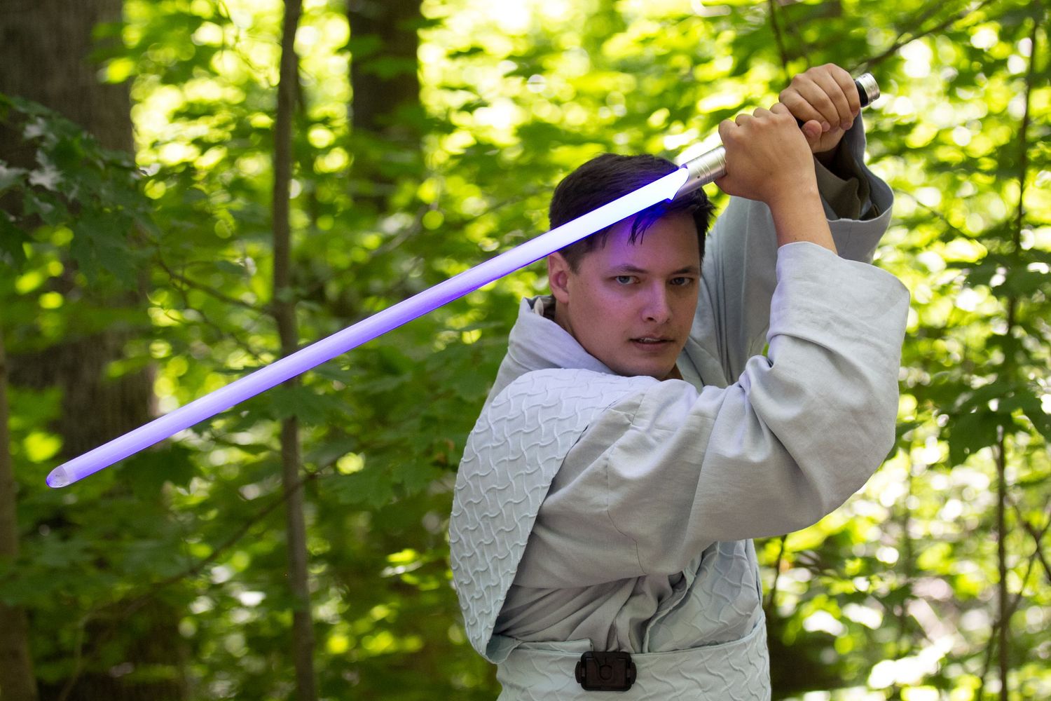 A figure in white robes wielding a blue lightsaber in a forest setting.