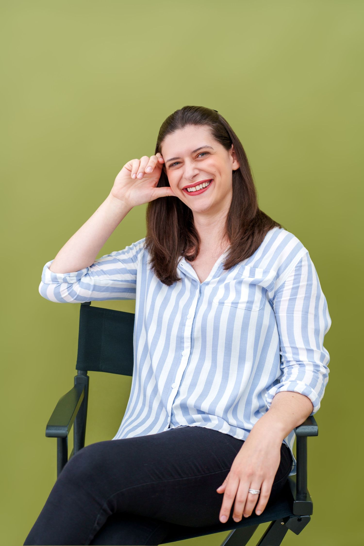 A person in a striped shirt sits relaxed in a director's chair against a green background.