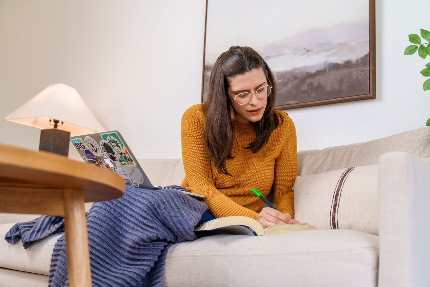 Person in yellow sweater reading while relaxing on white couch with plants in background.