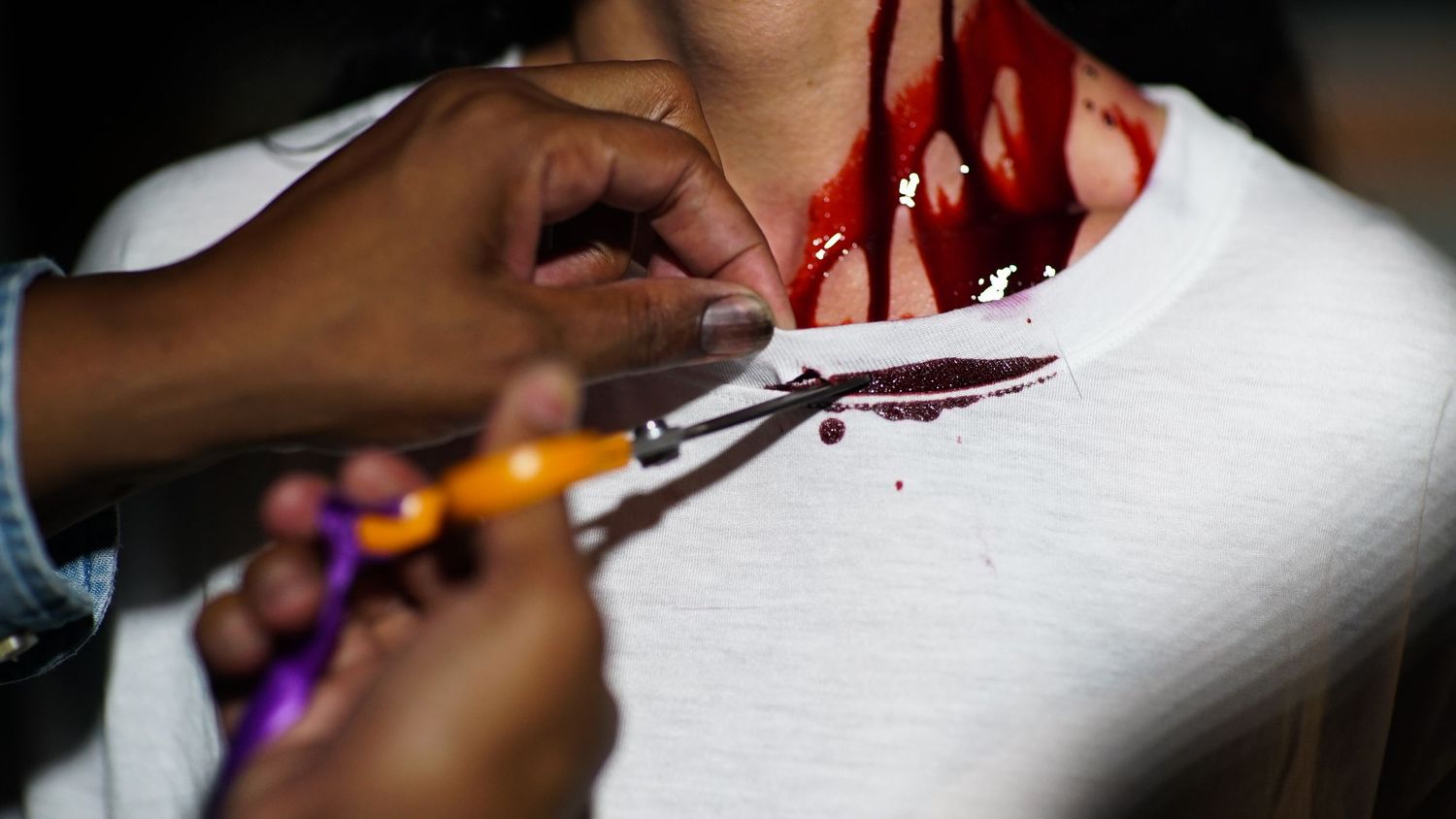 Special effects makeup artist applies fake blood and cuts to an actors neck on a film set.