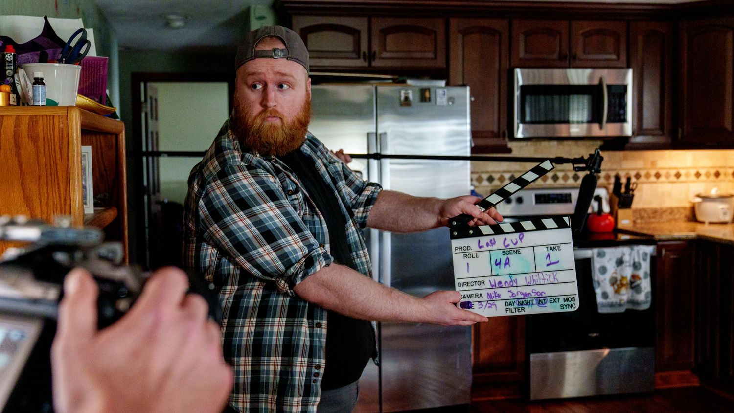 Man holding a film clapperboard on a movie set inside a kitchen during production.