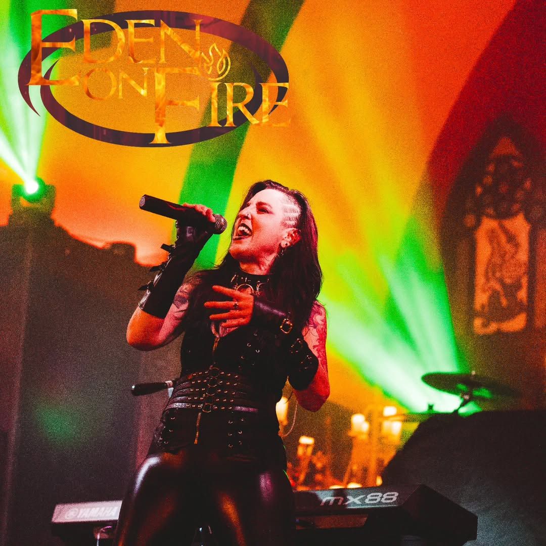 Concert performer singing passionately on stage with vibrant green and orange lighting effects in the background.