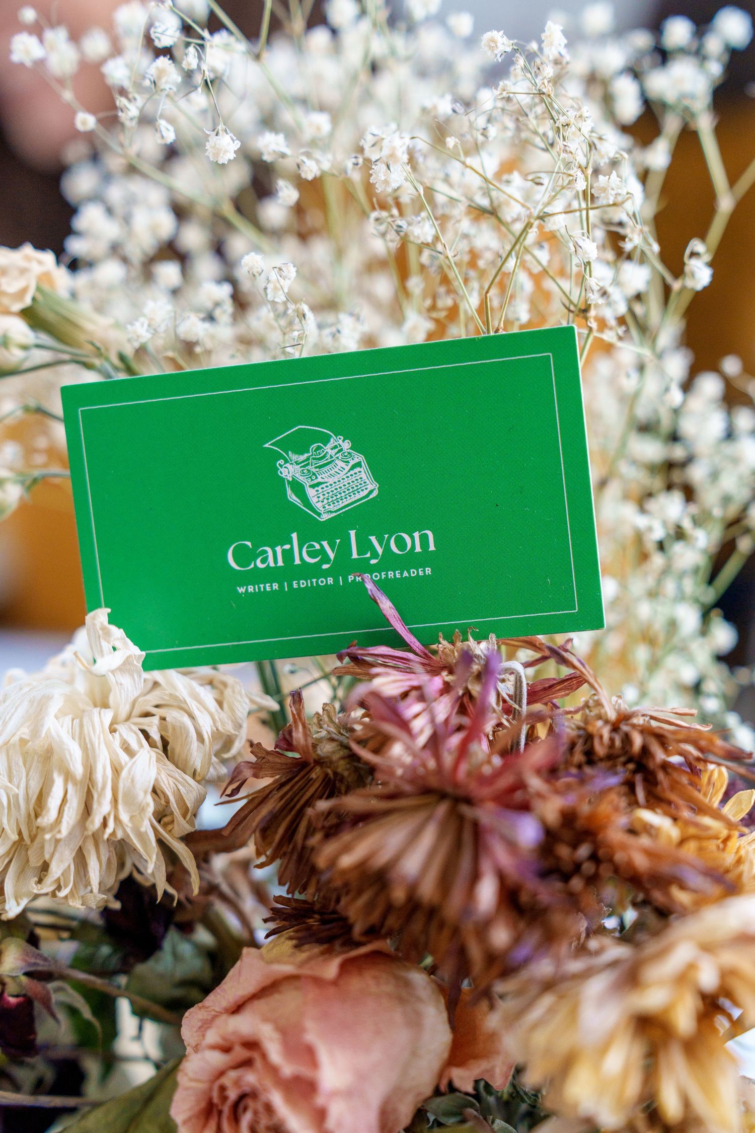 Green business card for Carley Lyon nestled among dried flowers and baby's breath.